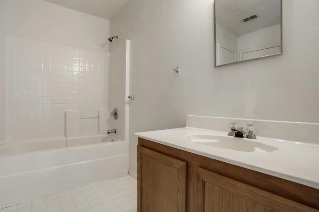 White subway tile tub surround, chrome fixtures, built-in vanity with wood-finish cabinetry, white countertop, and tile flooring