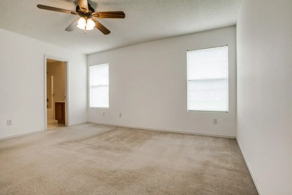 Spacious room with two windows, a ceiling fan with integrated lighting, and neutral-toned carpeting