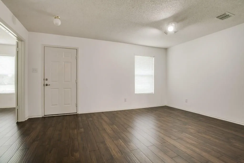 Wood-finish flooring, white walls, paneled door, ceiling-mounted lighting, and window with blinds