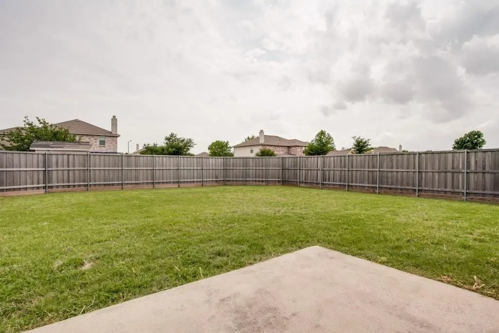 Expansive backyard featuring a manicured lawn, a full wood fence, and a concrete patio