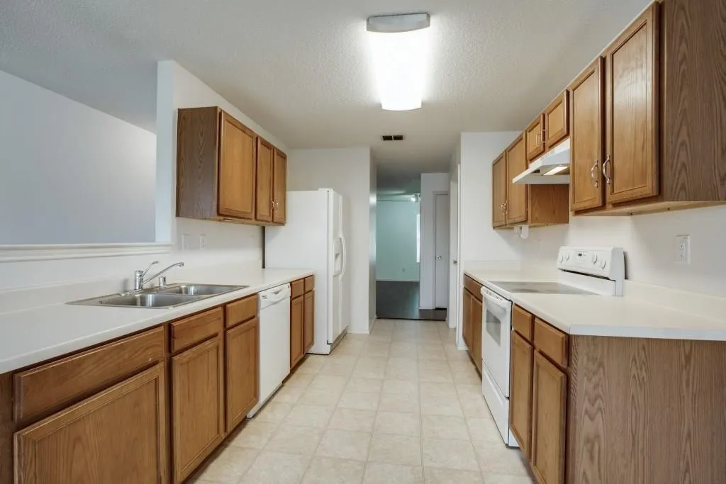 Galley kitchen featuring wood-finish cabinetry, white countertops, and white appliances