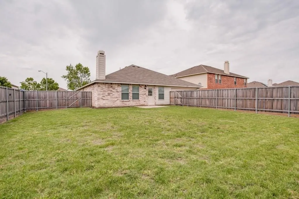Expansive backyard featuring a privacy fence, brick exterior, and a chimney