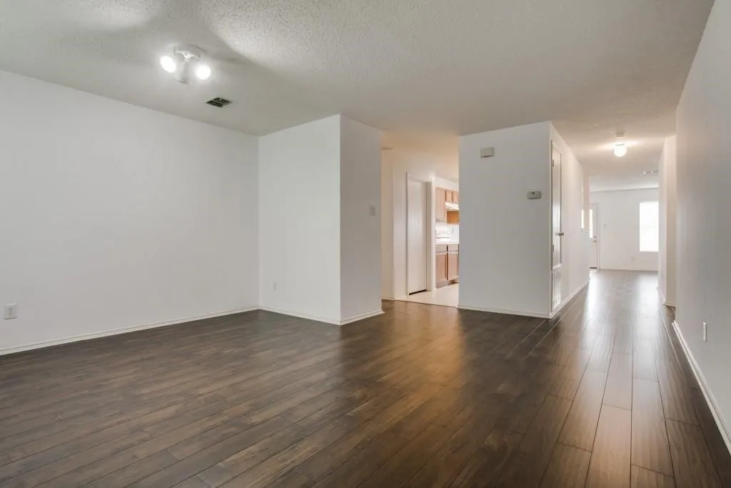 Spacious room with dark wood-finish flooring, white walls, and a track lighting fixture