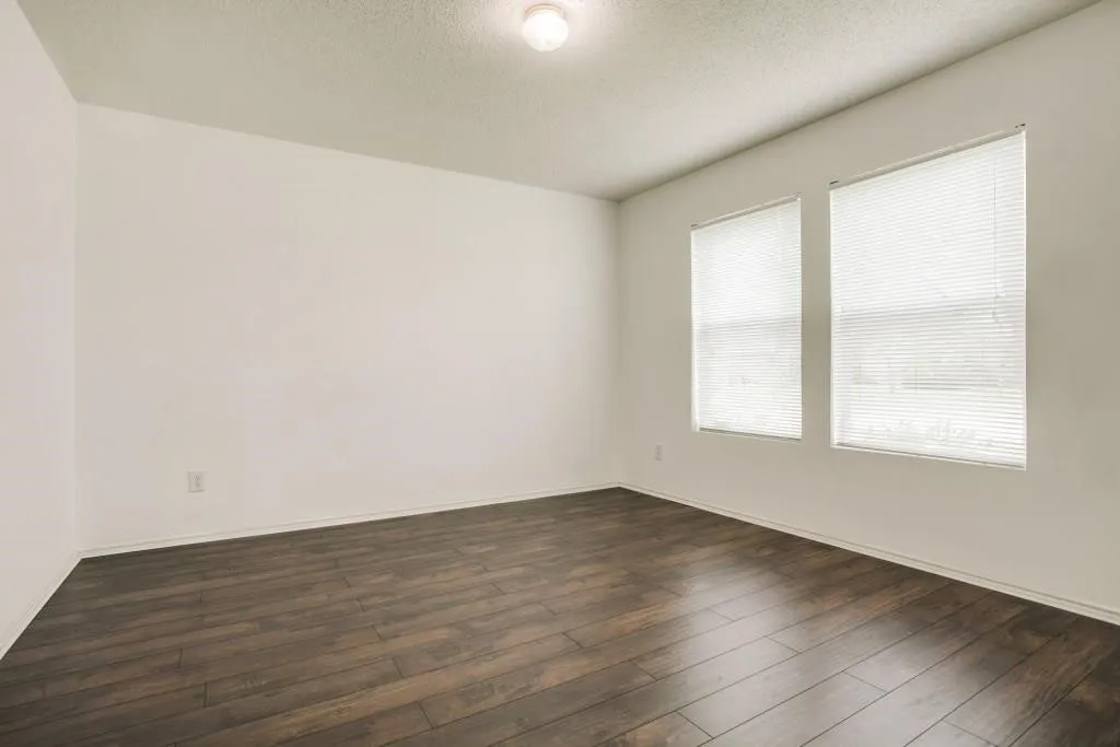 Wood-finish flooring with white walls, two windows with blinds, and a ceiling-mounted light fixture