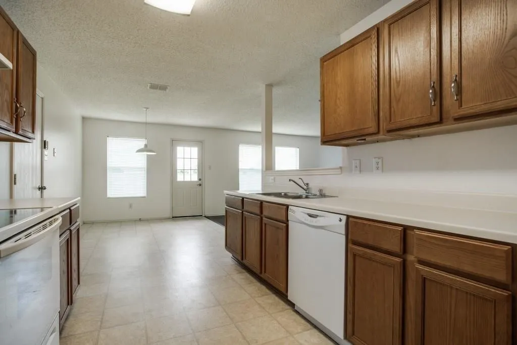 Kitchen featuring wood-finish cabinetry, white countertops, a built-in dishwasher, and a stainless steel sink