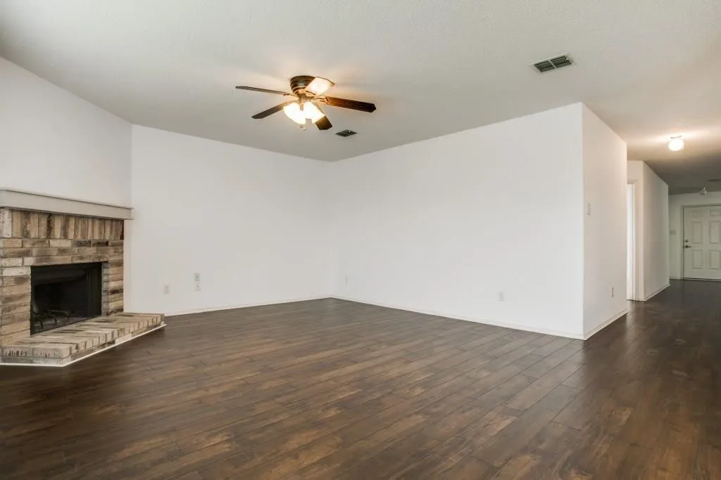Expansive living area featuring wood-finish flooring, a brick-surround fireplace with hearth, and a ceiling fan
