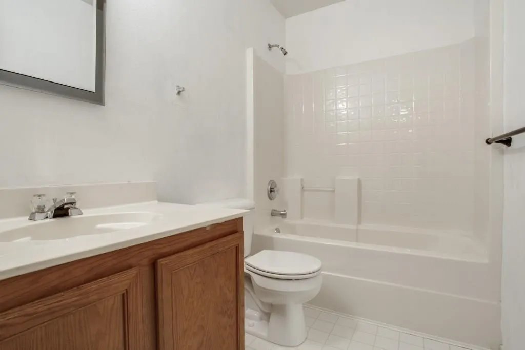 Bathroom featuring a wood-finish vanity with an integrated sink, a white countertop, and a white tiled shower/tub combination