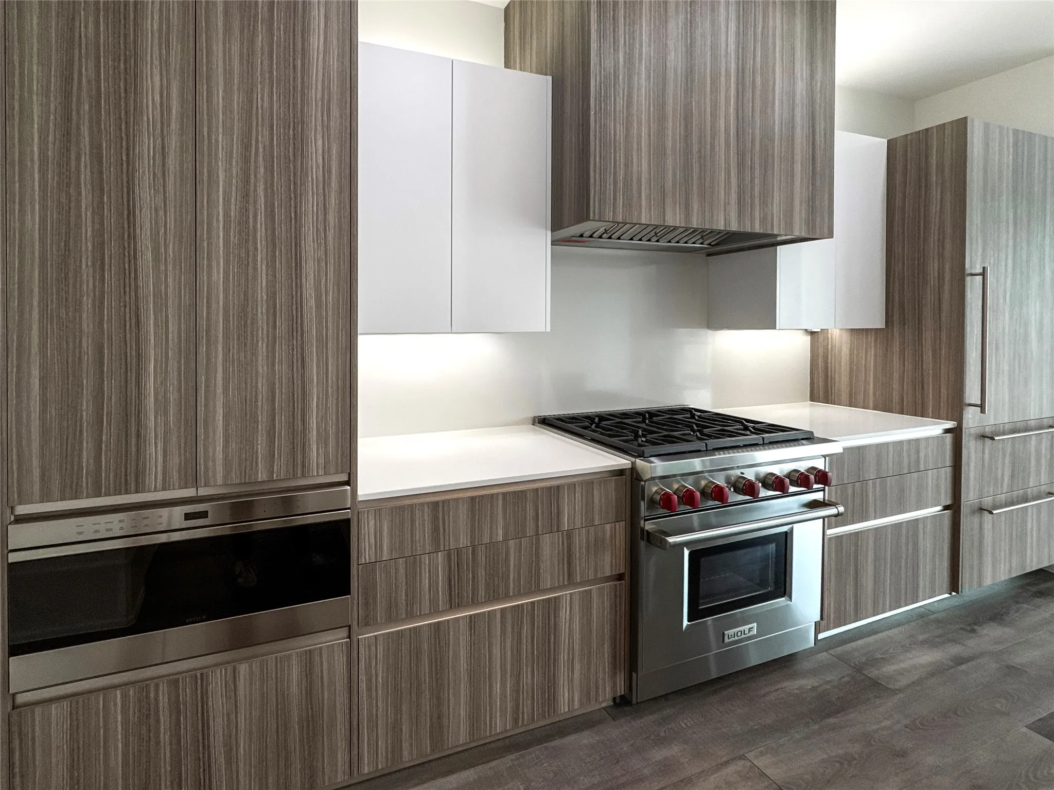 Kitchen with stainless steel appliances, white cabinetry, dark hardwood / wood-style floors, and ventilation hood
