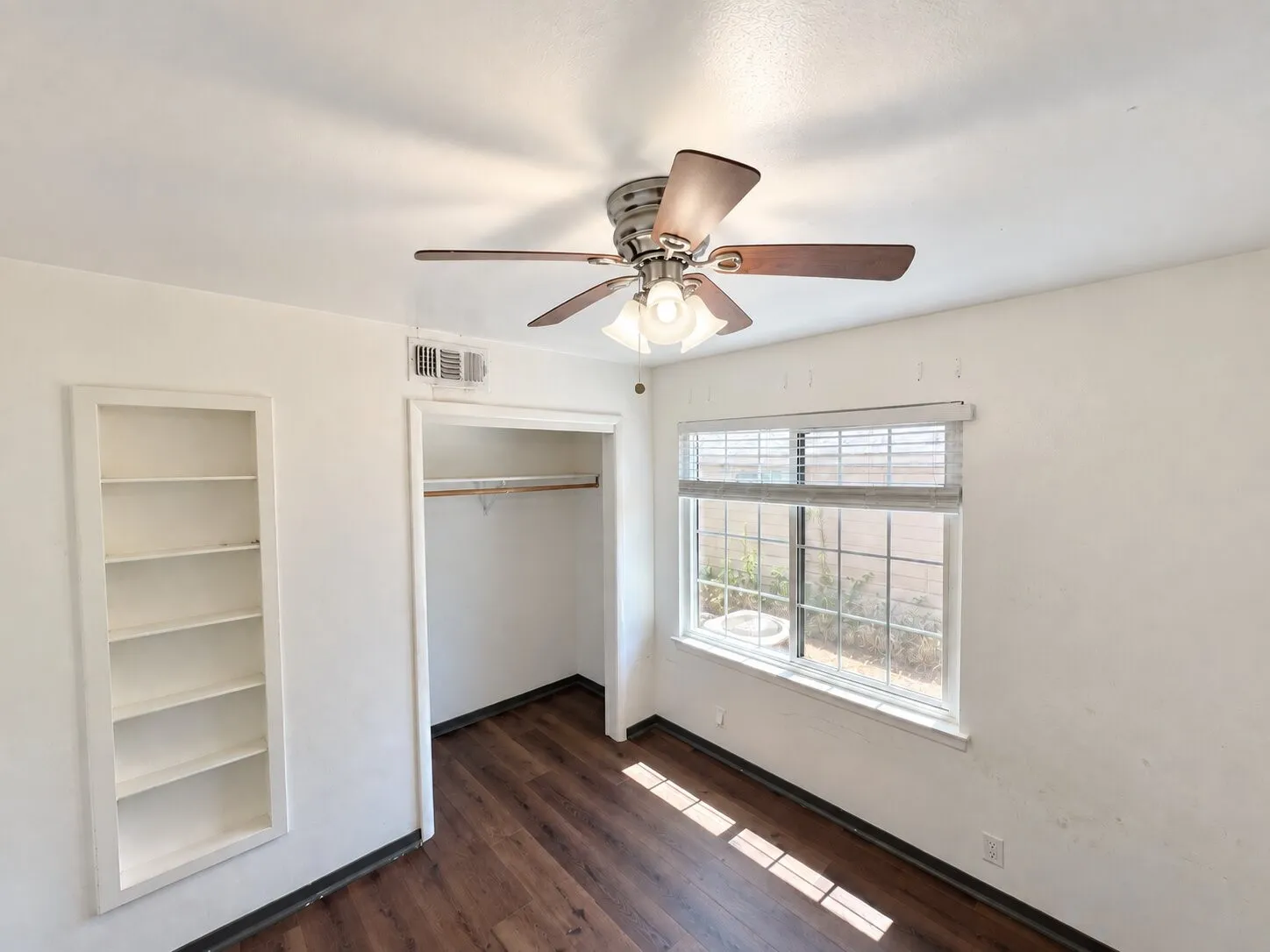 Virtually staged -
Built-in shelving, a closet with a hanging rod, a window with blinds, wood-finish flooring, and a ceiling fan with integrated lighting