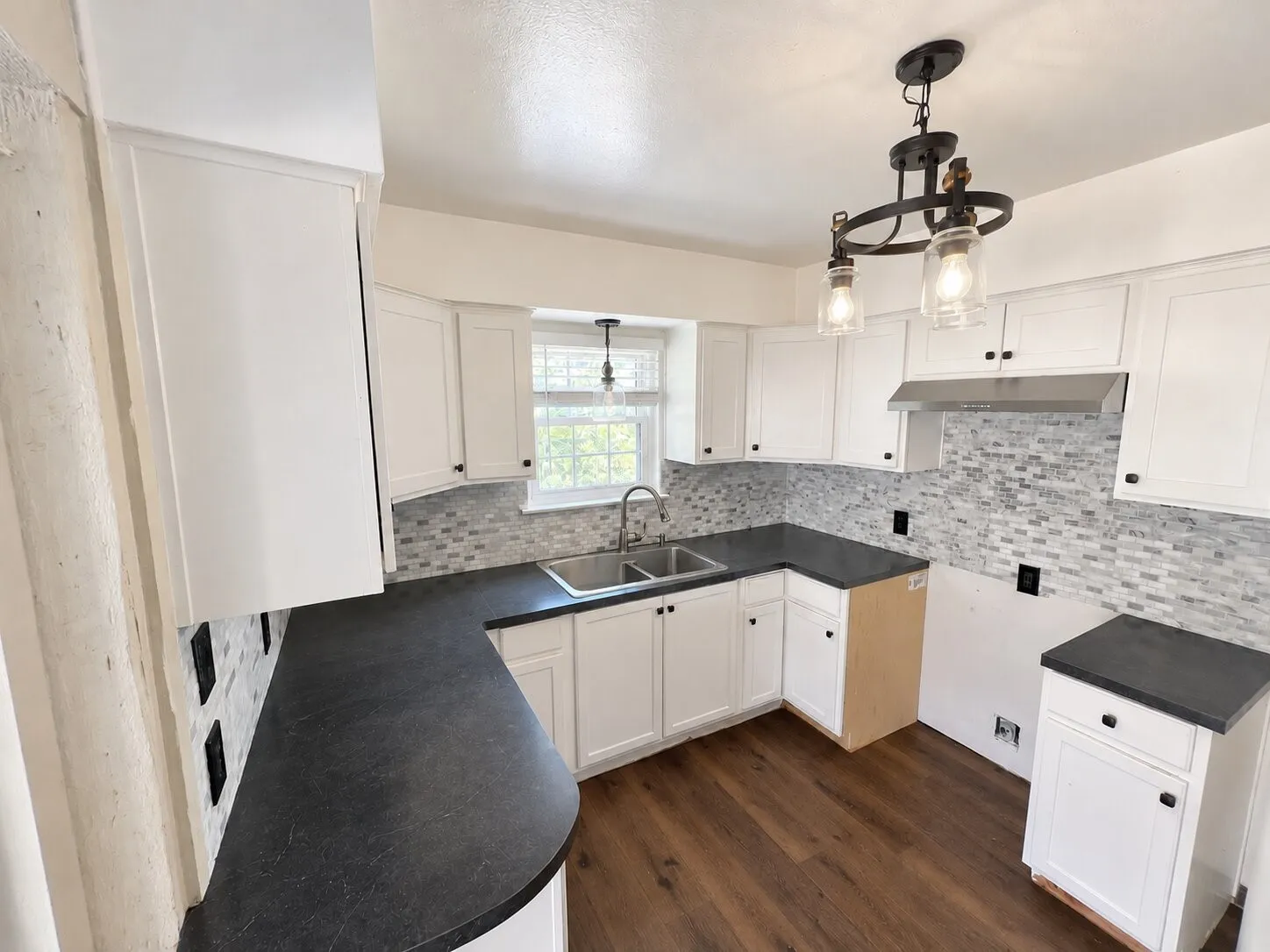 White cabinetry, dark countertops, tile backsplash, wood-finish flooring, and a ceiling-mounted light fixture