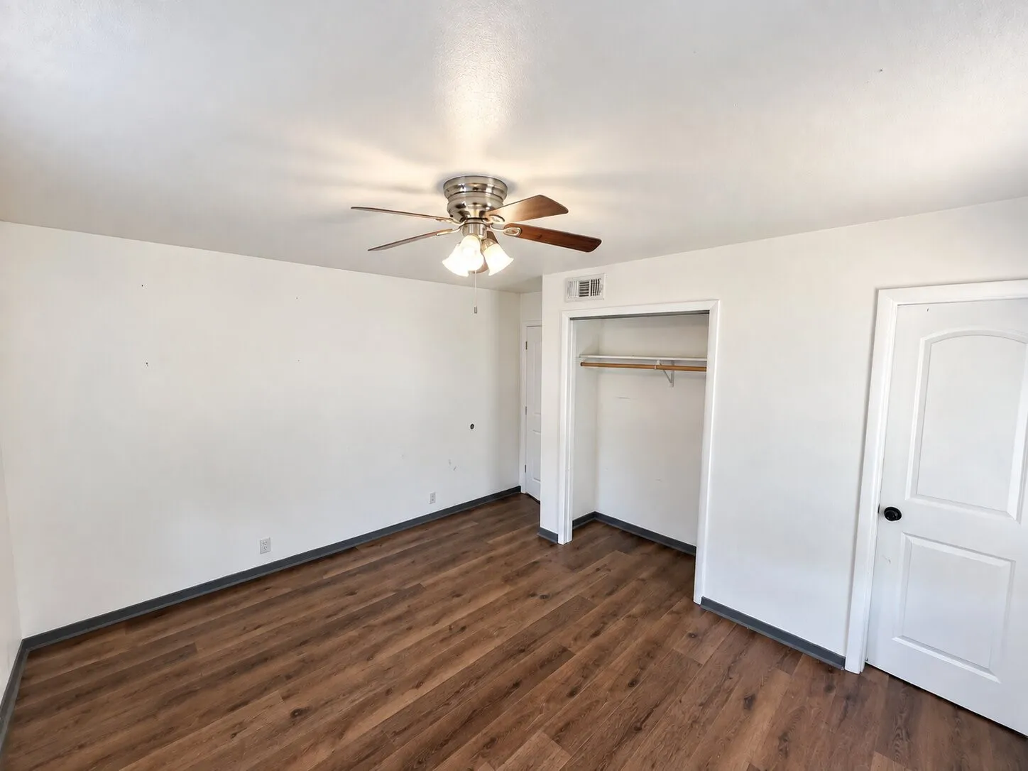 Wood-finish flooring, ceiling fan with integrated lighting, white interior door with black hardware, and an open closet with a built-in hanging rod