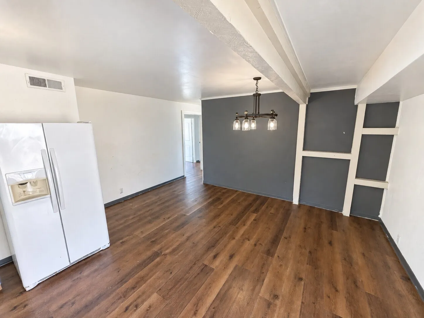 Wood-finish flooring, exposed ceiling beams, modern chandelier, accent wall with decorative paneling