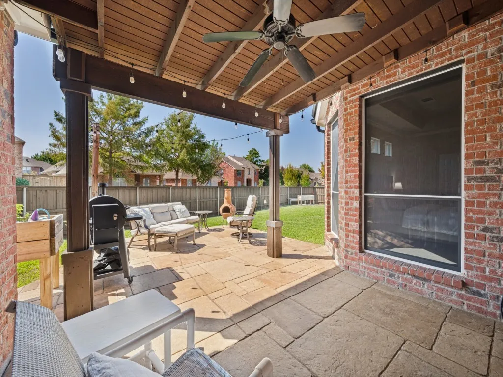 The covered patio provides a comfortable outdoor living space overlooking the expansive grassy backyard, offering plenty of room for relaxing, entertaining, and enjoying the outdoors.