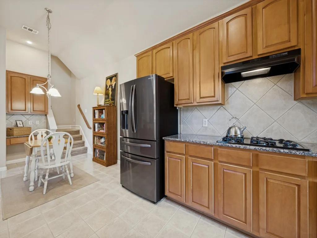 The spacious open kitchen showcases beautiful cherry cabinetry, granite countertops, black appliances, and a gas cooktop, offering a stylish and functional setting for cooking and entertaining.