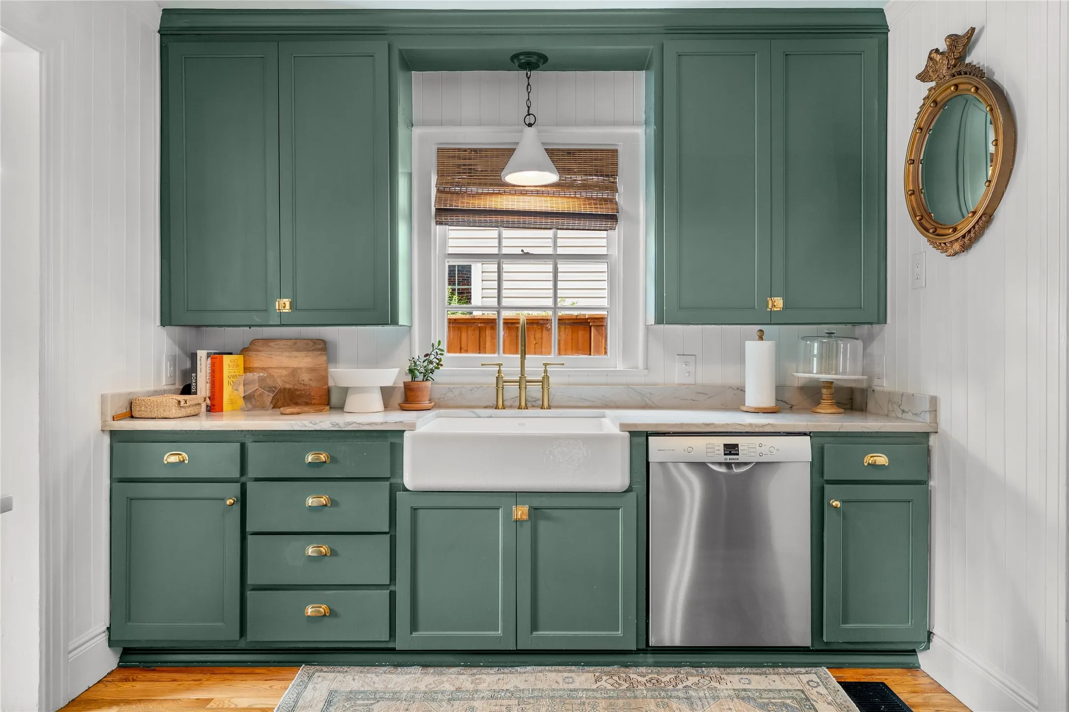 Custom cabinetry with brass hardware, a farmhouse-style sink, gold-finish faucet, and stainless steel dishwasher