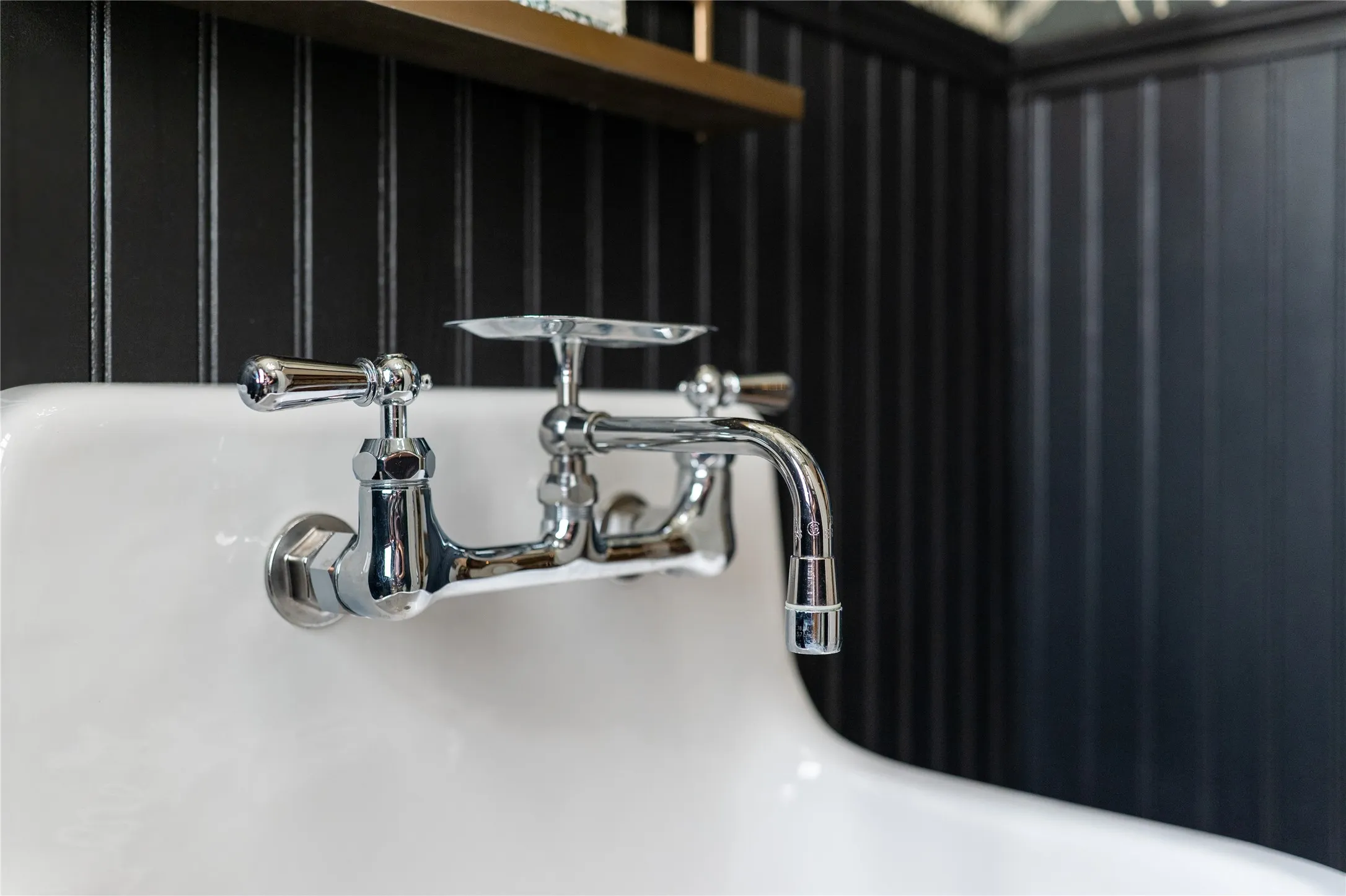 White wall-mounted sink with chrome faucet, featuring black vertical paneling and a brass-tone shelf