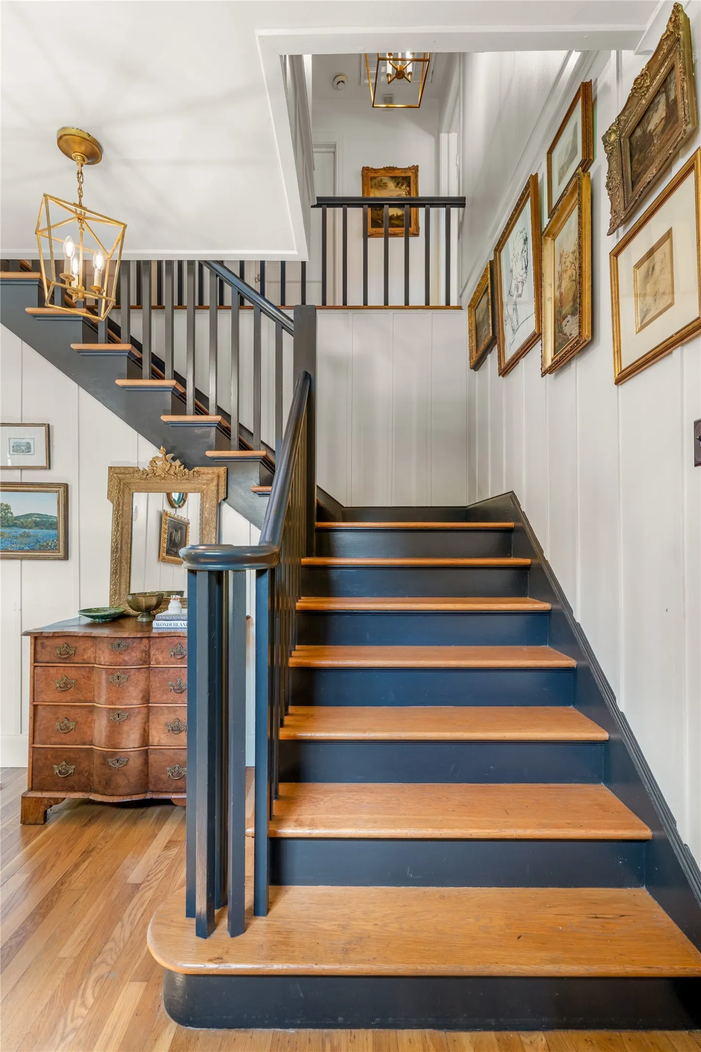 Hardwood flooring, painted risers, wood treads, painted balusters, and a gold-finish geometric chandelier