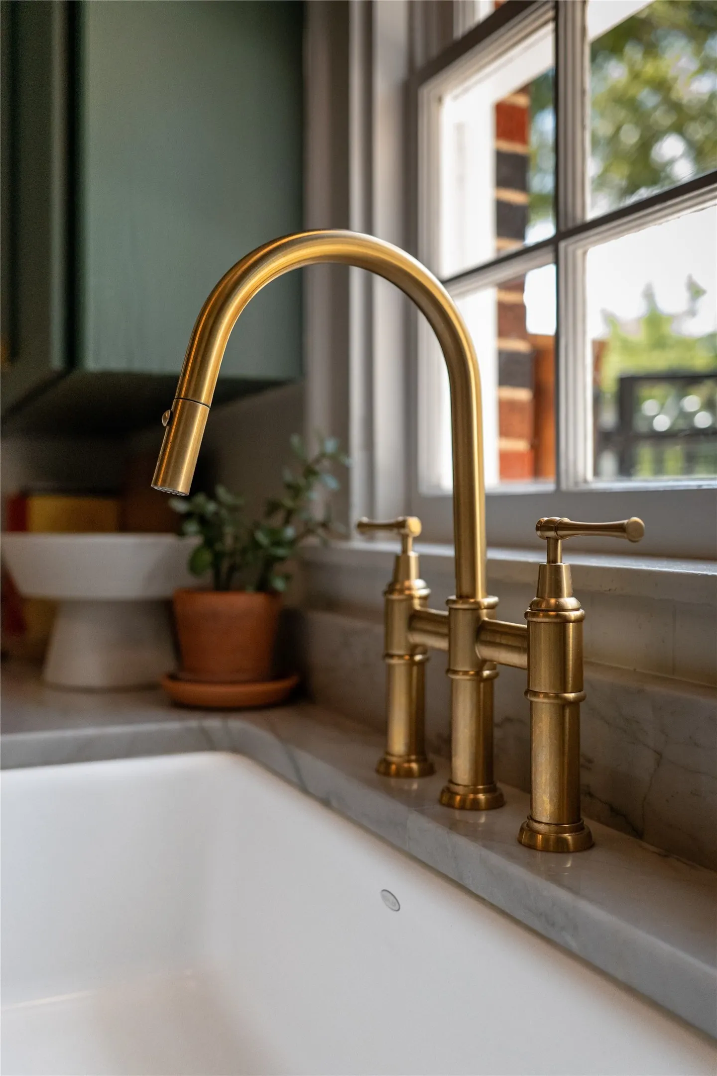 White undermount sink with a brass-finish pull-down faucet, set into a stone countertop