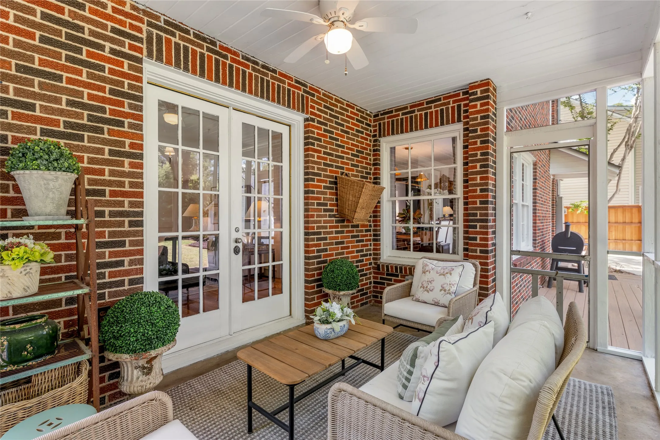 Enclosed porch featuring brick walls, white French doors, a ceiling fan, and a screened opening to an exterior deck