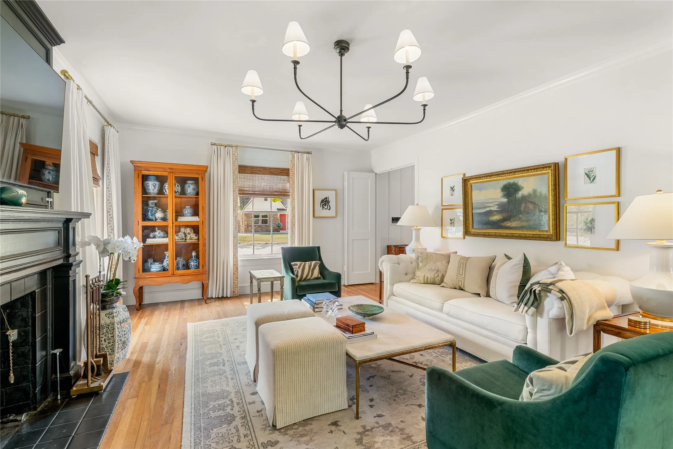 Hardwood flooring, crown molding, a built-in fireplace with a dark tile surround, a chandelier light fixture, and window treatments with blinds