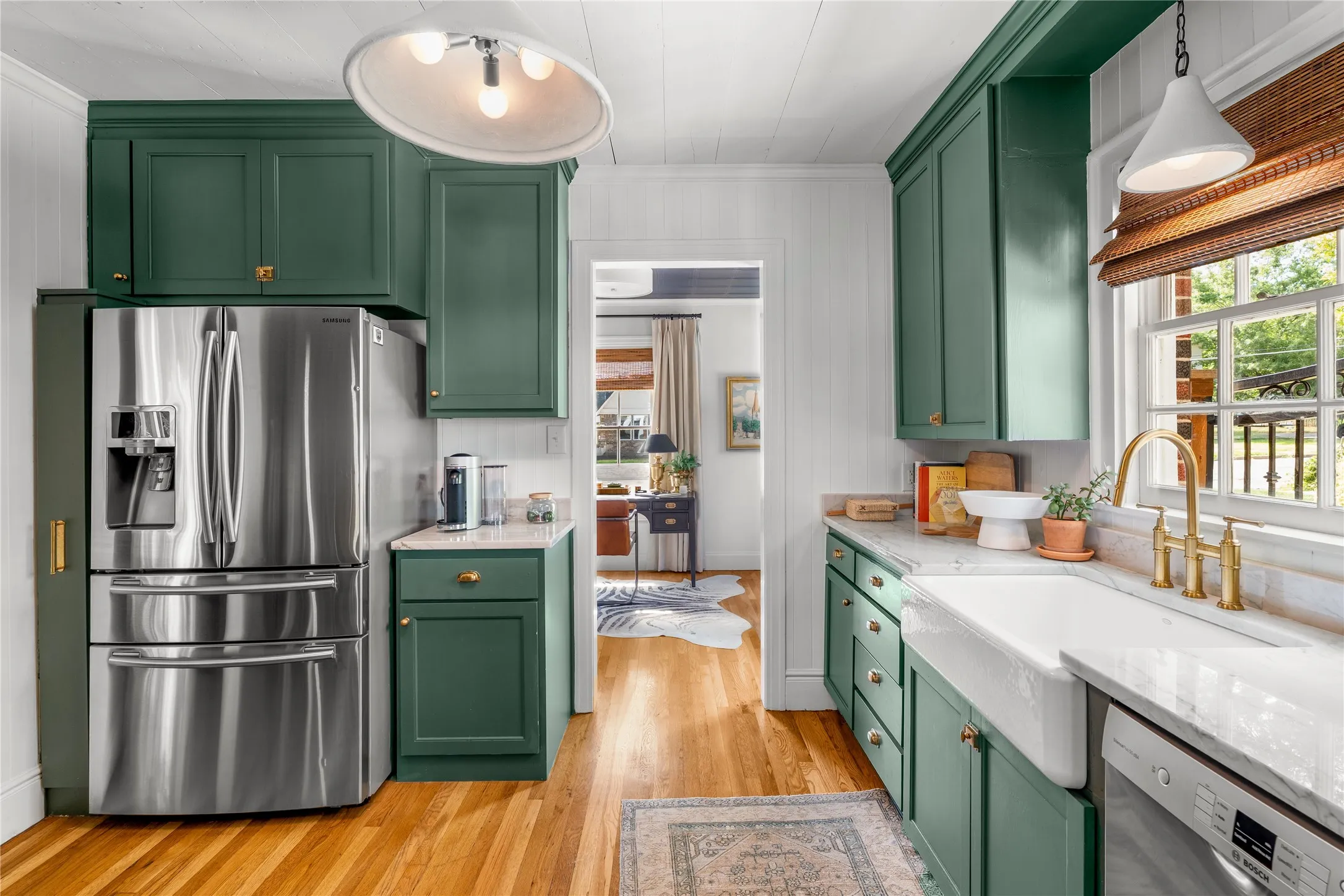 Kitchen featuring rich green cabinetry, hardwood flooring, an integrated refrigerator, a farmhouse sink, and a brass-finish faucet