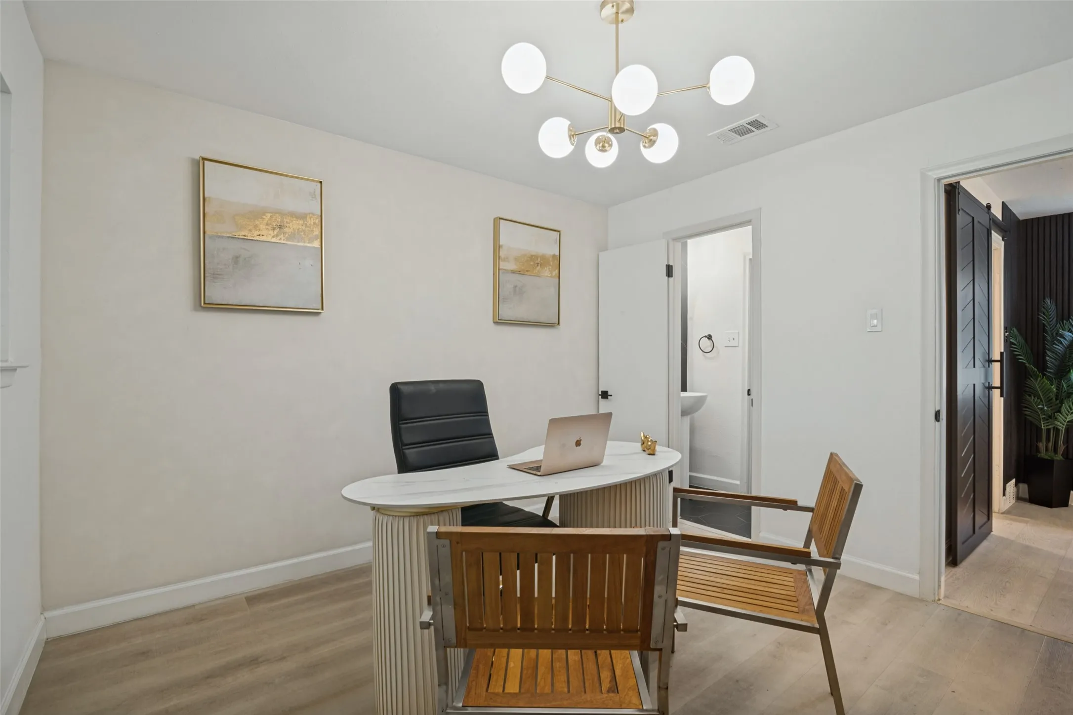 Modern chandelier, light wood-finish flooring, white walls, and dark wood barn door