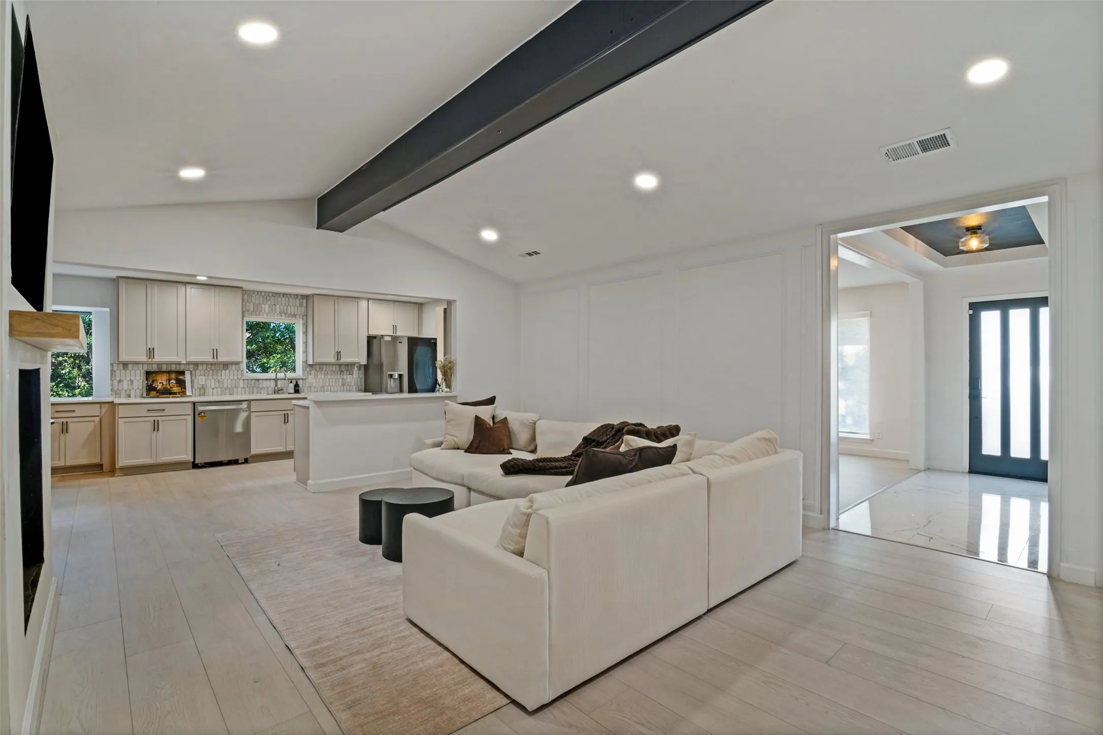 Vaulted ceiling with an exposed beam, light wood-finish flooring, recessed lighting, and a modern kitchen with stainless steel appliances and light cabinetry