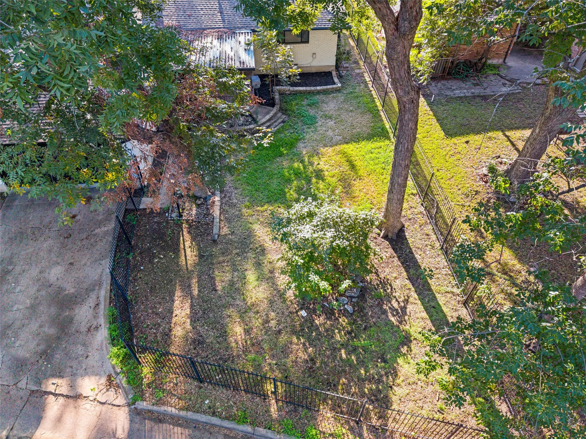 Rear yard featuring mature trees, a black metal fence, and a concrete pathway