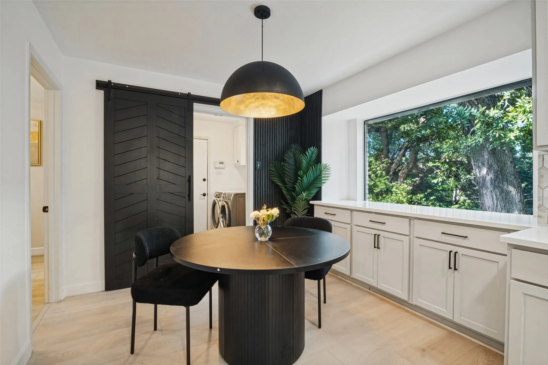 Wood-finish flooring with a modern black barn door, a contemporary dome pendant light, integrated window bench seating, and white cabinetry with dark hardware