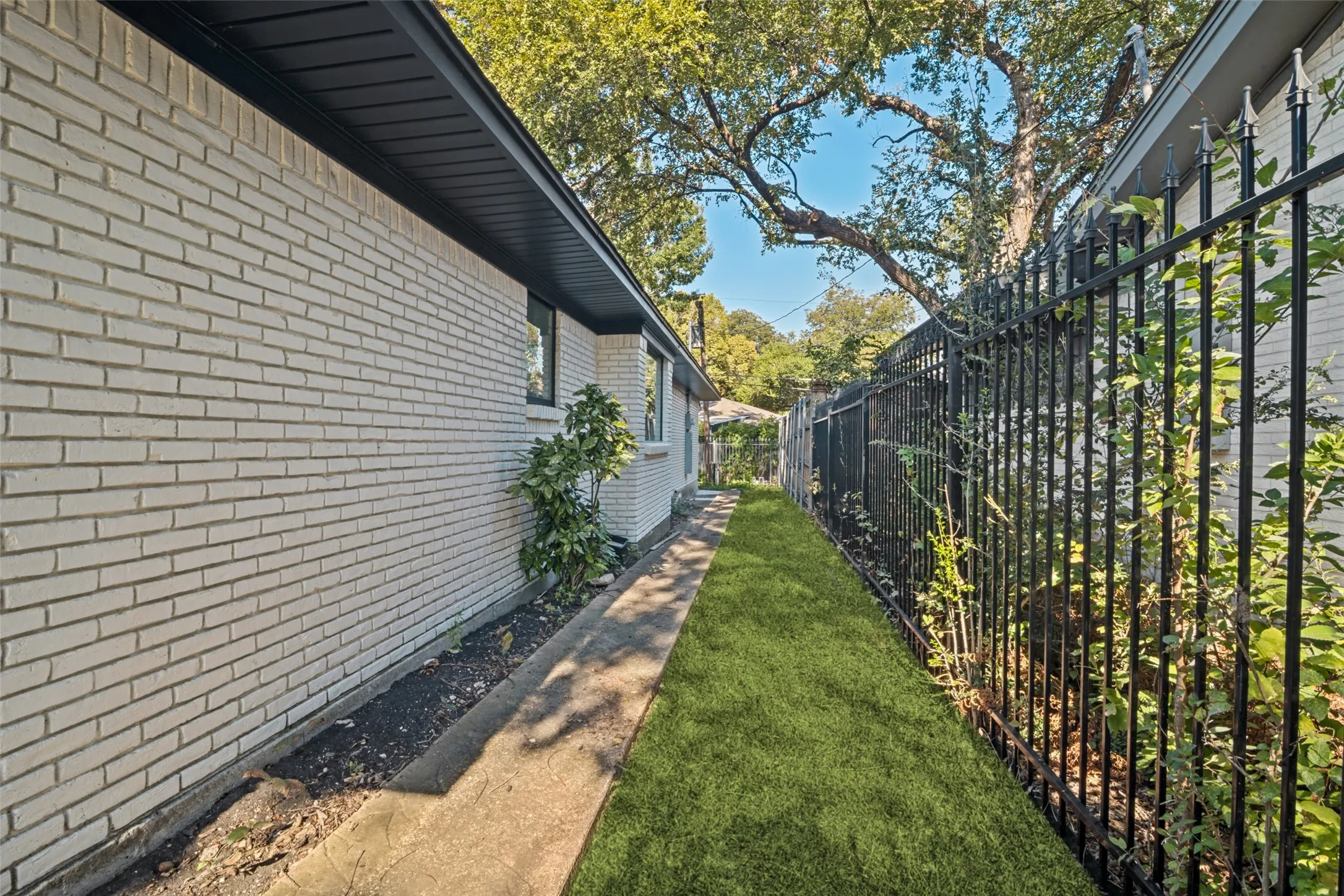 White brick exterior, black soffit, black window trim, concrete pathway, and black metal fencing