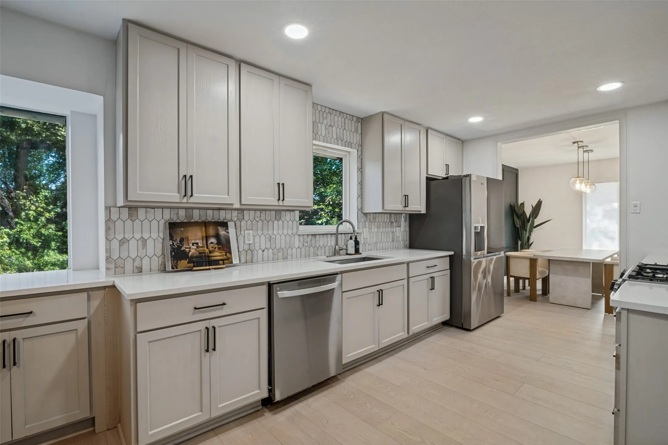 Contemporary kitchen featuring light wood-finish flooring, white cabinetry with black hardware, white countertops, and a patterned tile backsplash