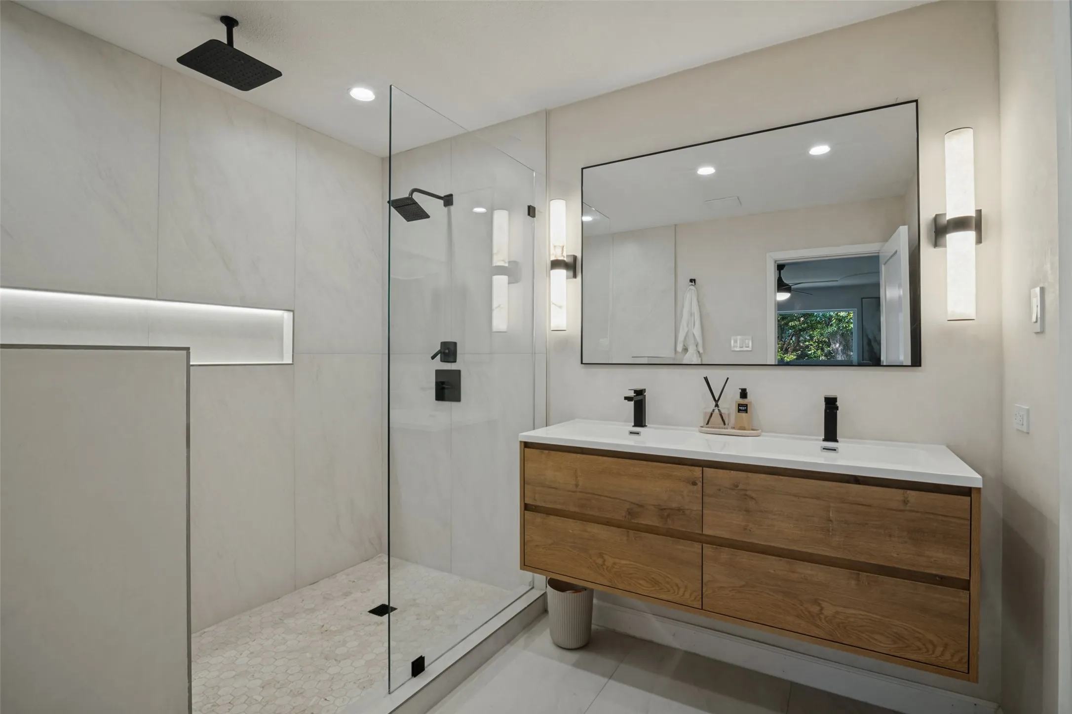 Dual-sink floating vanity with wood-finish cabinetry, frameless mirror, and modern sconces
