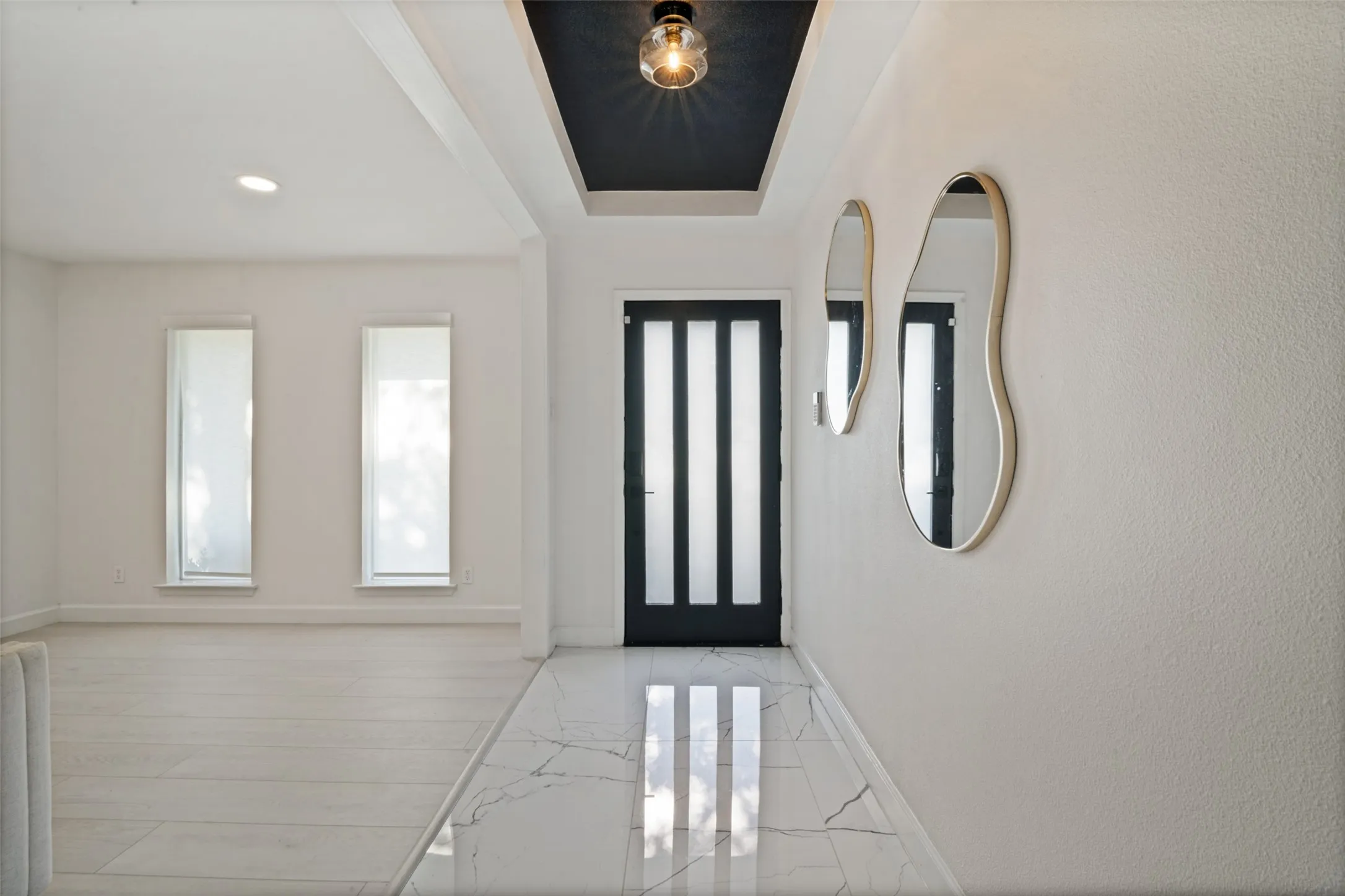 Recessed ceiling lighting, a dark contrasting ceiling accent, and a modern entry door with vertical light panels