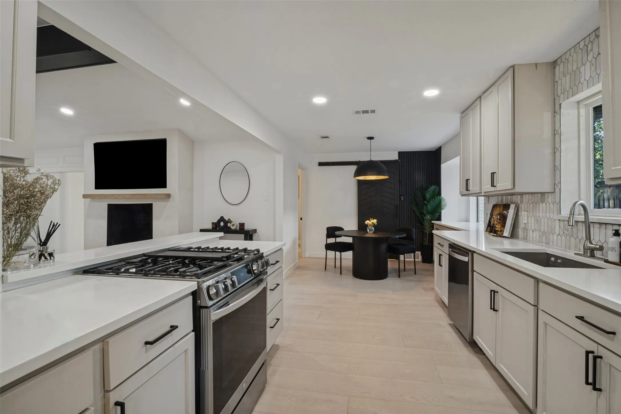 Modern kitchen with light-toned wood-finish flooring, white cabinetry, integrated stainless-steel appliances, and a unique tiled backsplash