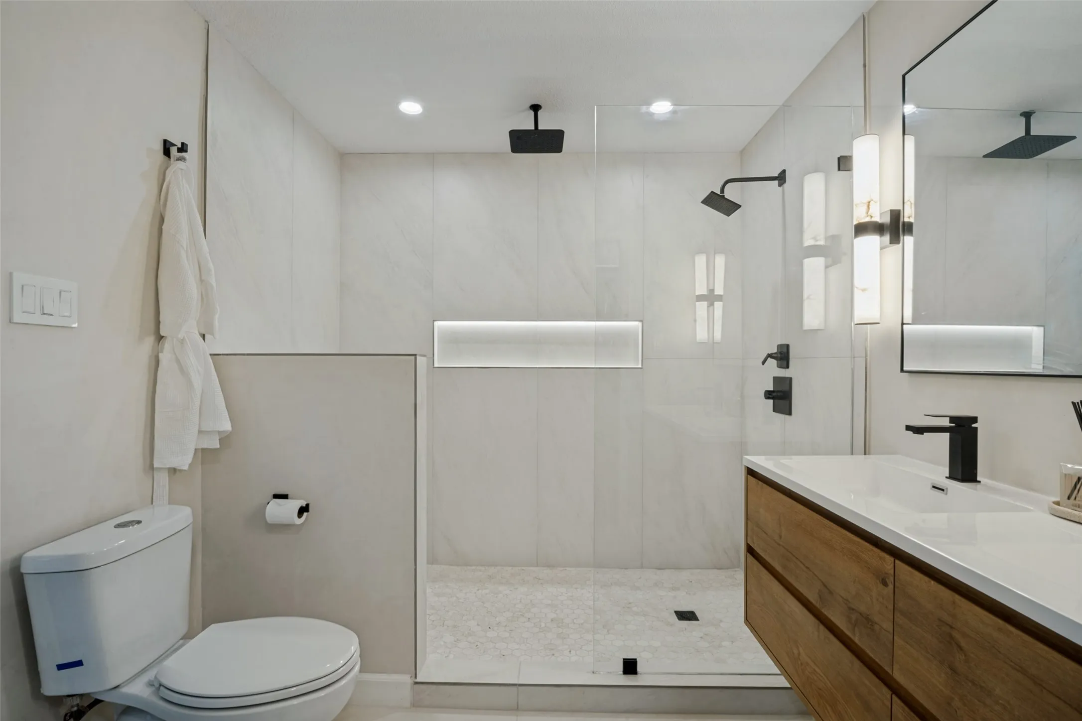 Spa-inspired primary bathroom featuring a spacious walk-in shower with frameless glass enclosure, dual rainfall showerheads, and linear niche shelving