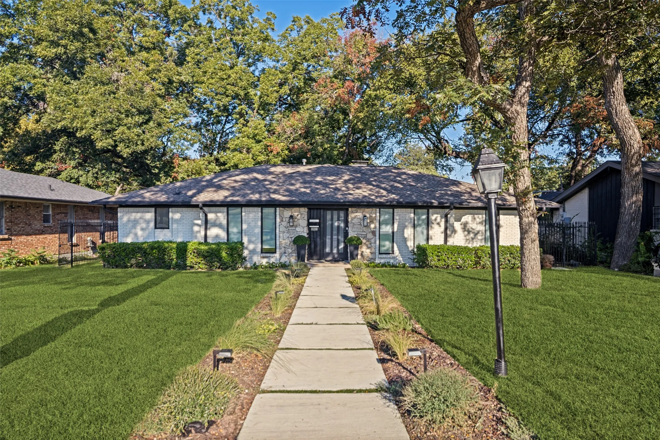 White stone and stucco exterior with dark trim windows, a dark shingle roof, a dark entry door, and a concrete paver walkway