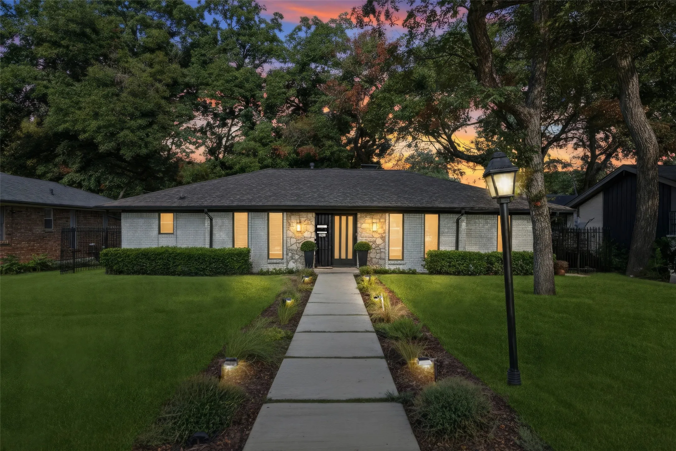 Modern ranch-style residence featuring a dark shingle roof, stone and stucco exterior, and a concrete paver walkway