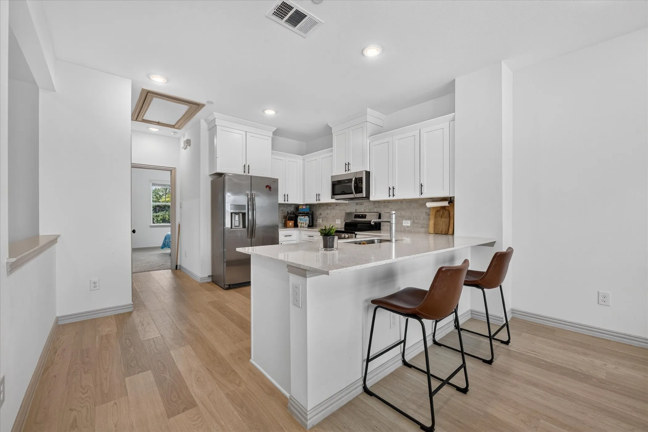 White cabinetry with brushed nickel hardware, stainless steel appliances, light-toned wood-finish flooring, and a breakfast bar with a light-toned countertop