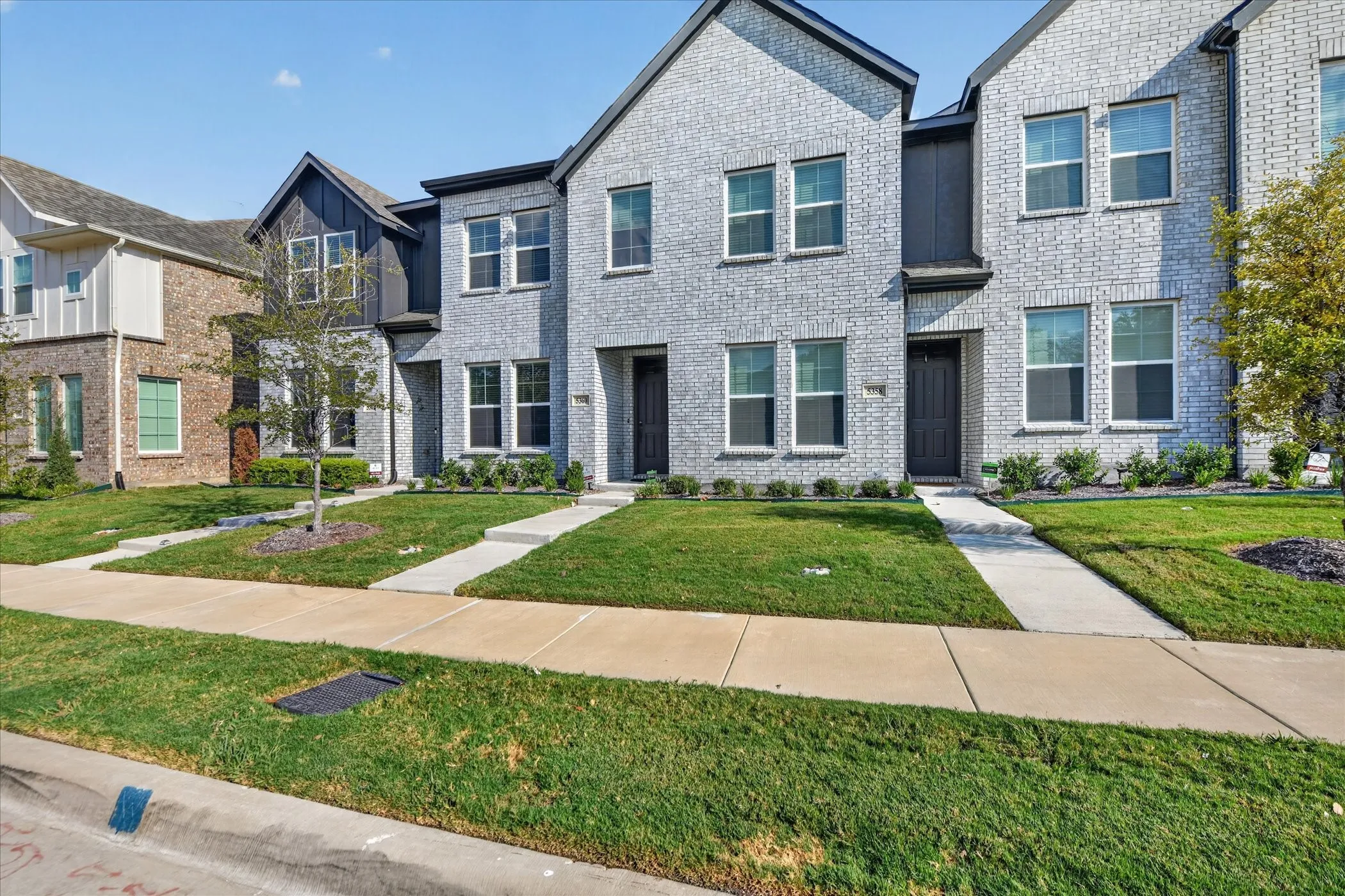 Gray brick facade with black trim accents, multiple windows, and a concrete walkway