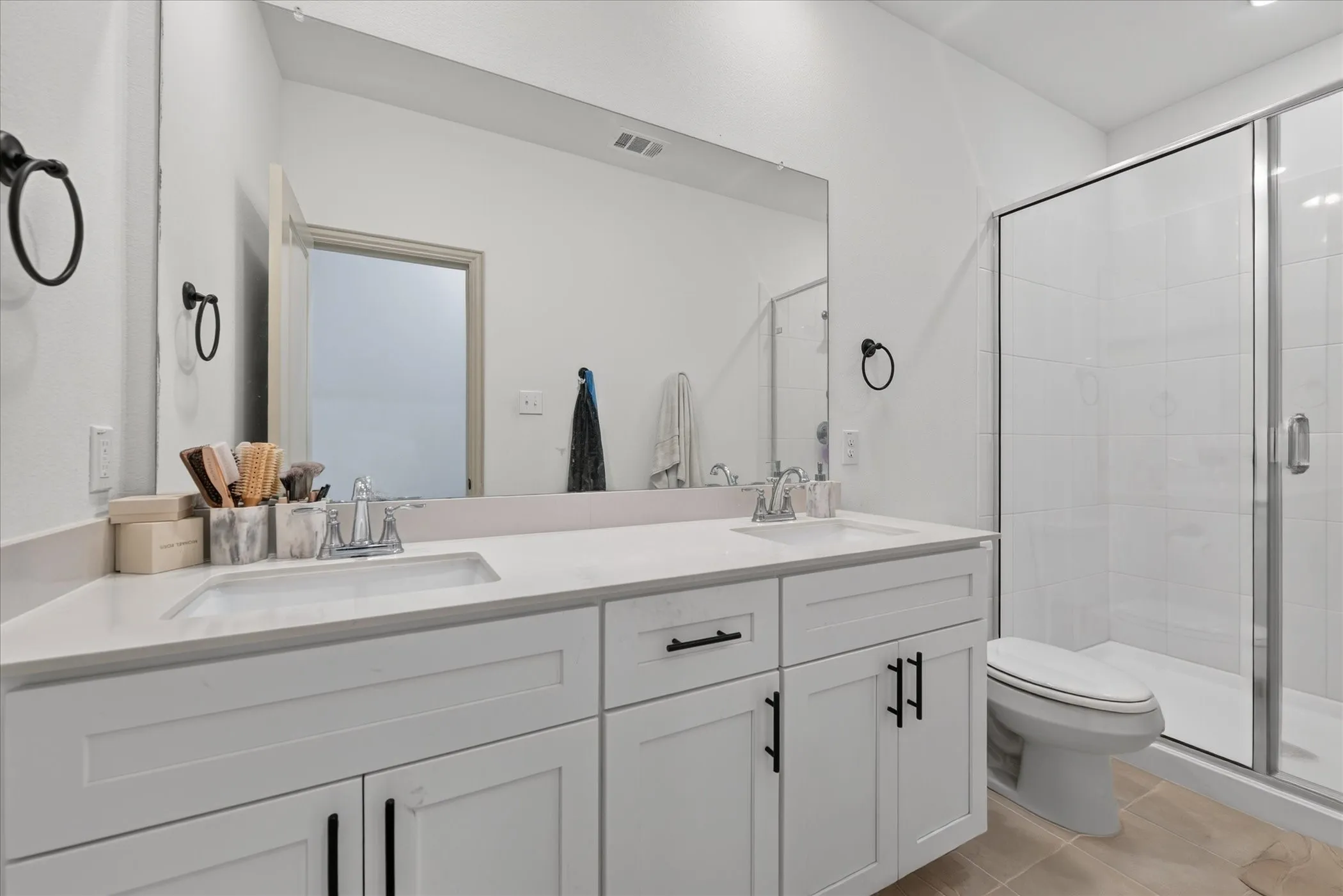 Dual vanity with an integrated countertop, white shaker-style cabinetry, matte black hardware, and a glass-enclosed shower