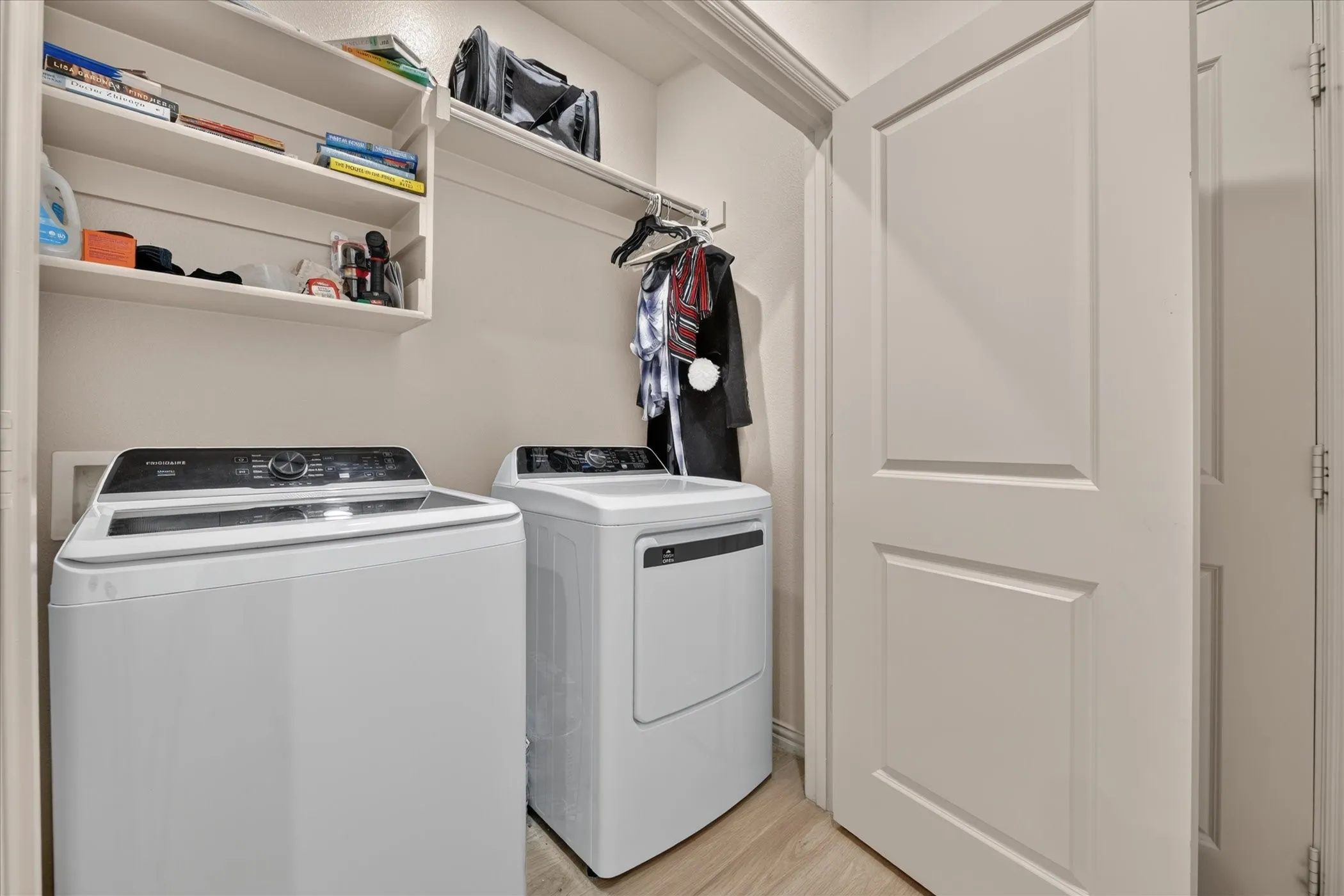 Laundry area with built-in shelving and hanging rod, complemented by a panel interior door and wood-finish flooring