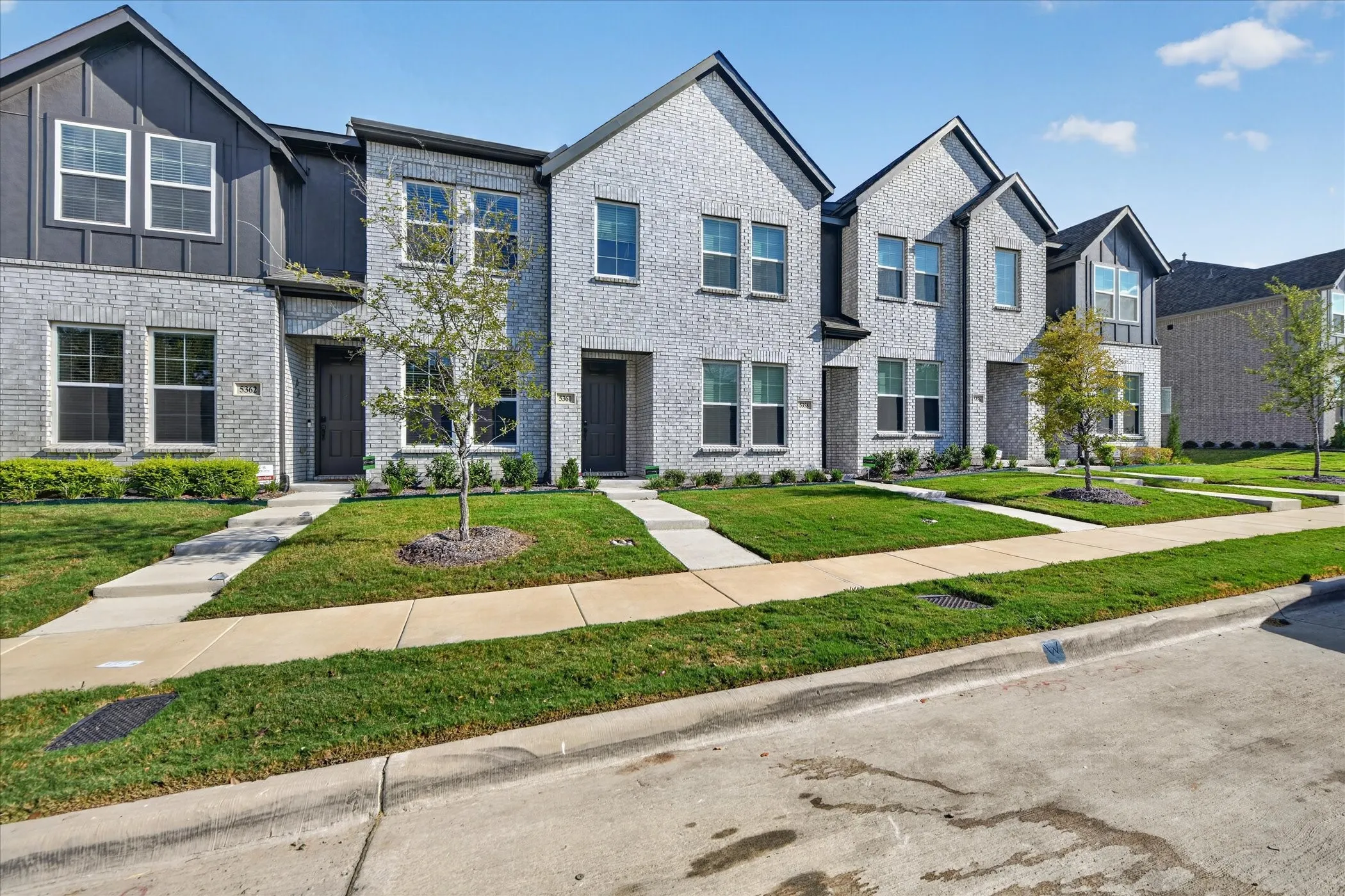 Modern townhome featuring a brick and board-and-batten facade, multiple windows, a prominent gabled roofline, and landscaped front yards