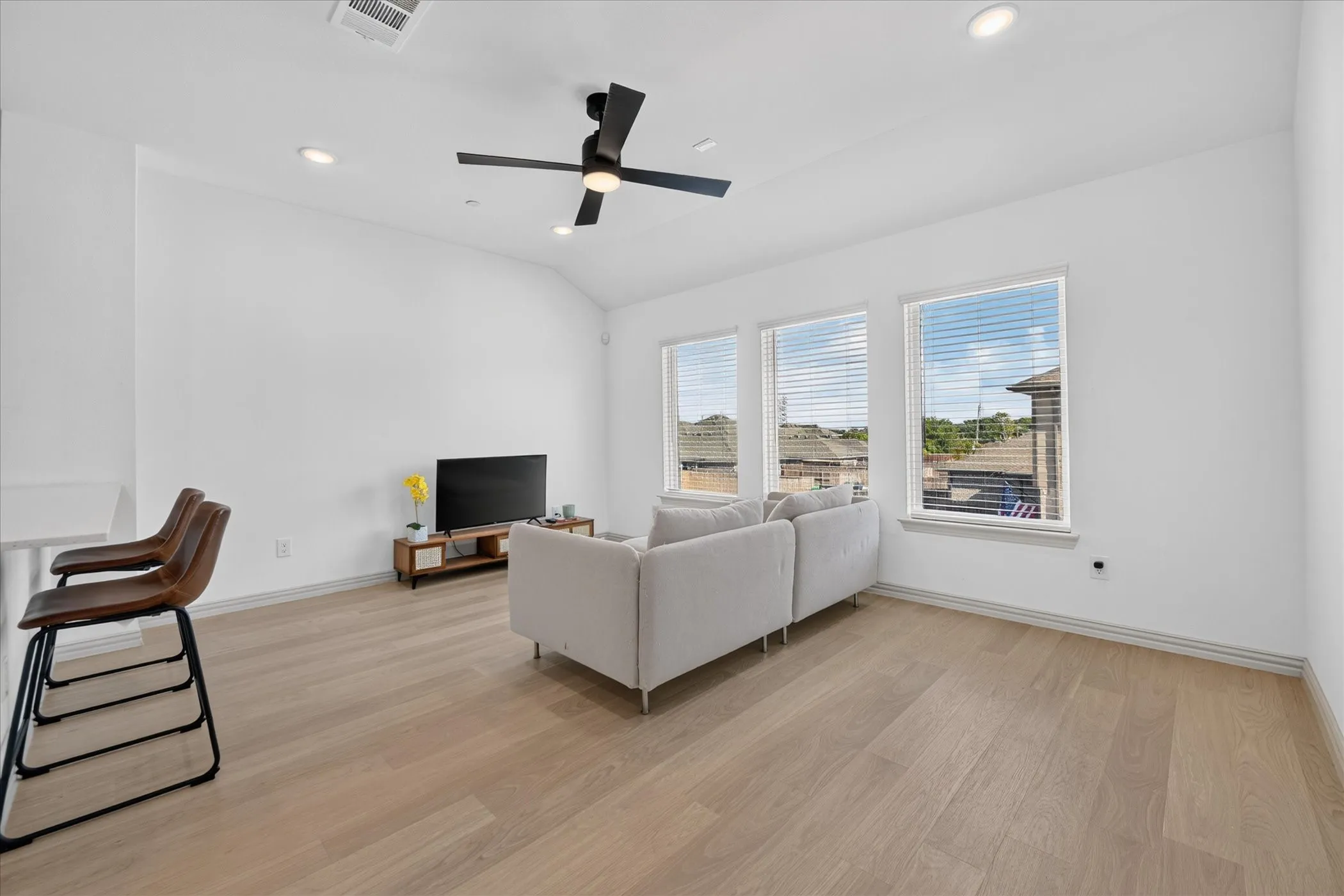 Bright living space featuring wood-finish flooring, recessed lighting, a ceiling fan, and multiple windows with blinds