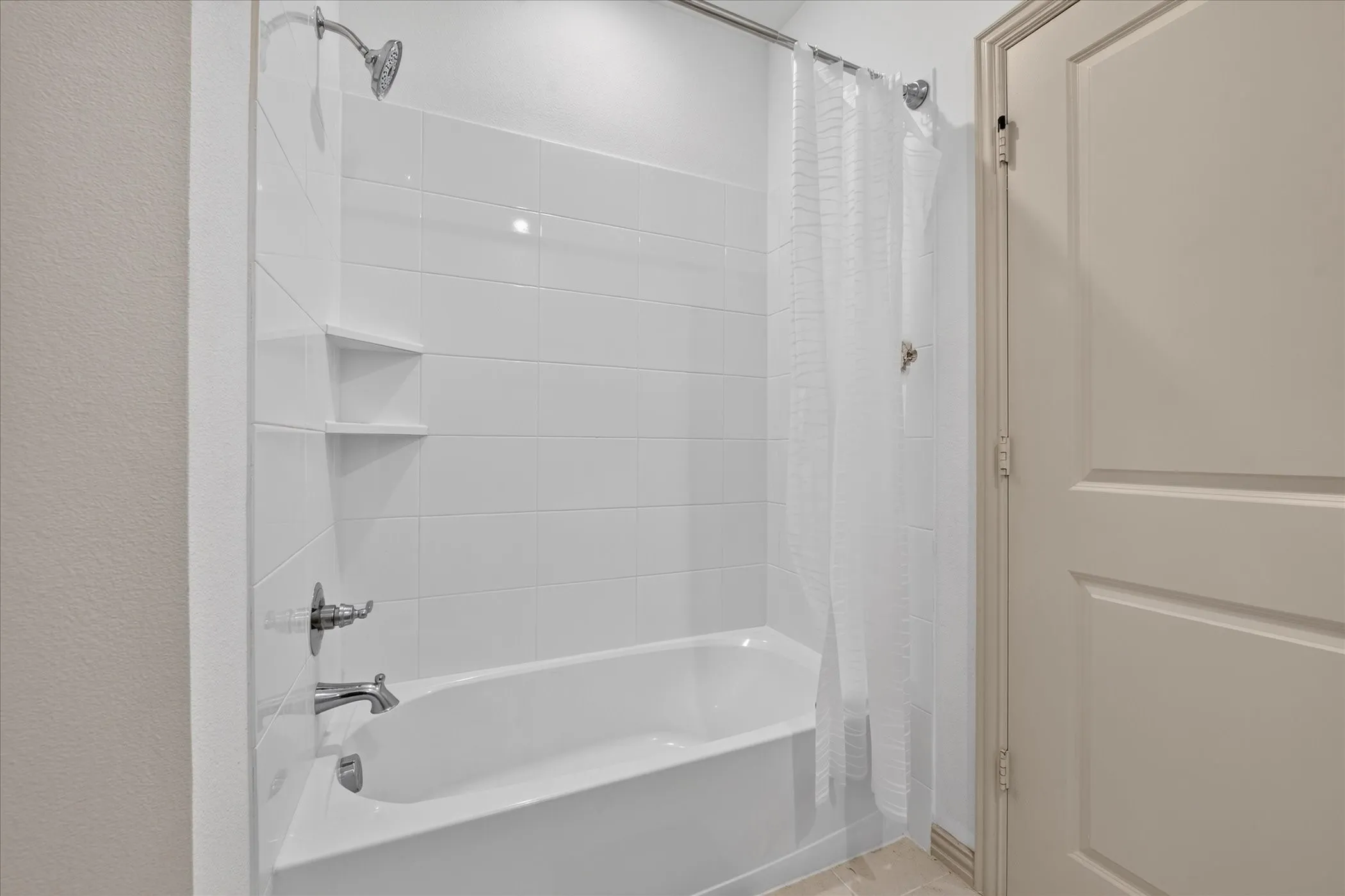 Built-in tub with white tile surround, integrated shelving, and chrome fixtures