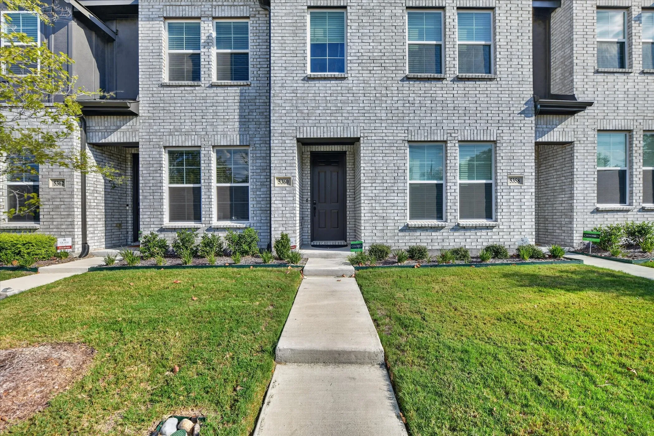 Contemporary brick facade, multiple double-hung windows, concrete walkway, established lawn, and landscaping