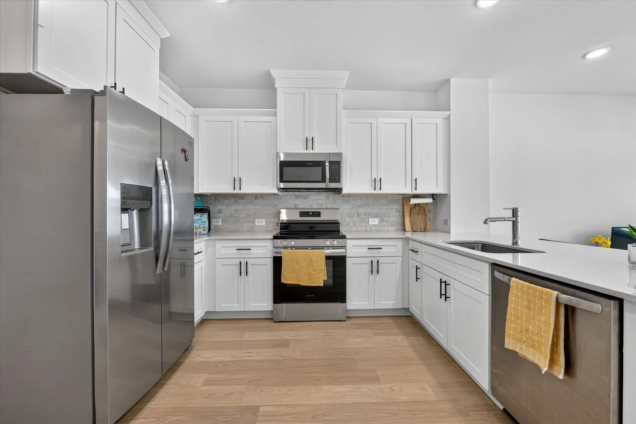 Kitchen featuring white cabinetry, stainless steel appliances, a tile backsplash, light-toned wood-finish flooring, and a single-basin sink