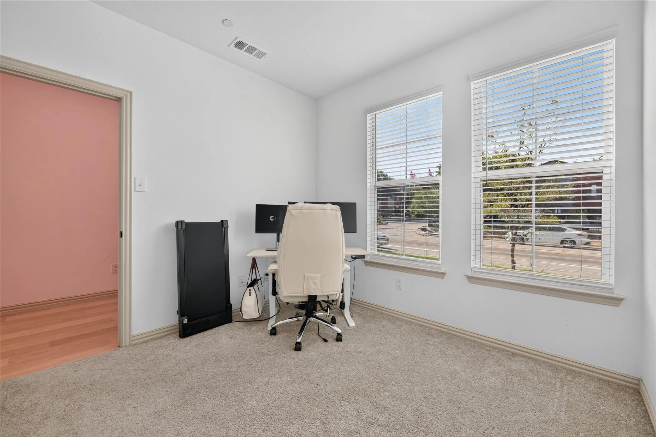 White walls, two large windows, neutral-toned carpet, and a light-colored door frame