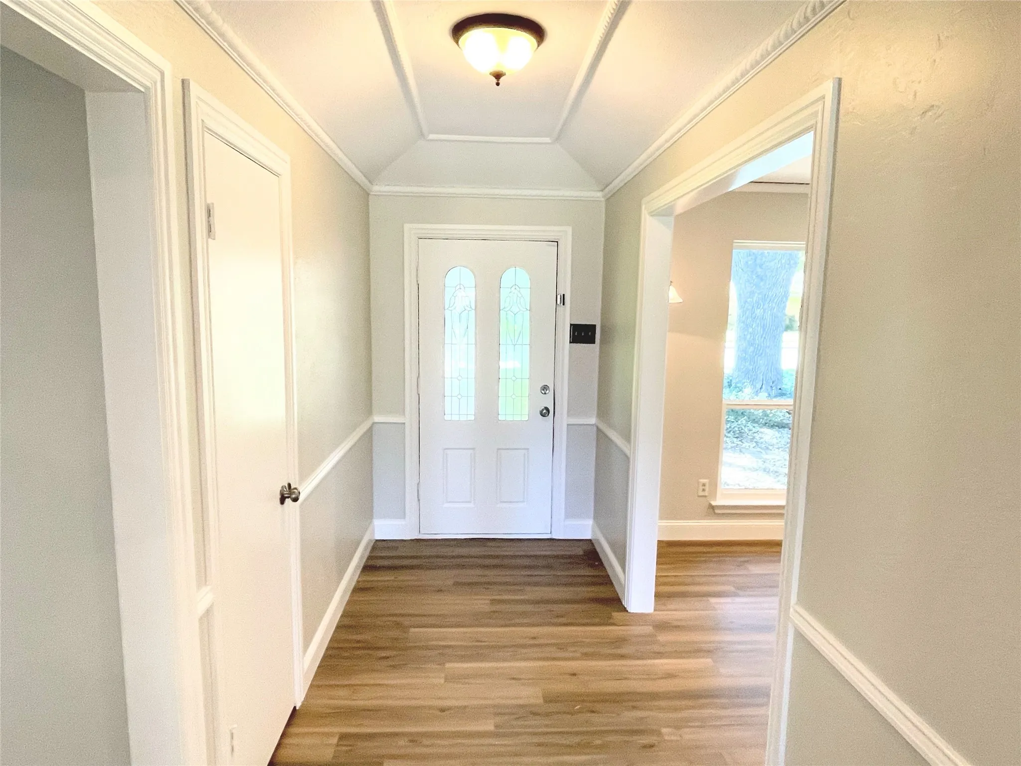Foyer entrance with ornamental molding, light hardwood / wood-style flooring, and vaulted ceiling