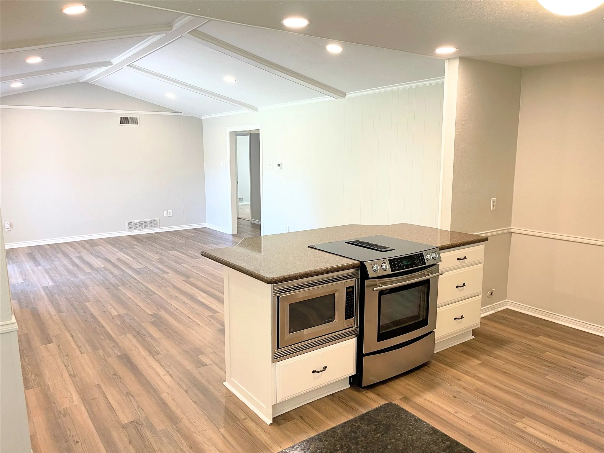 Kitchen with appliances with stainless steel finishes, dark stone countertops, white cabinets, lofted ceiling, and light hardwood / wood-style flooring