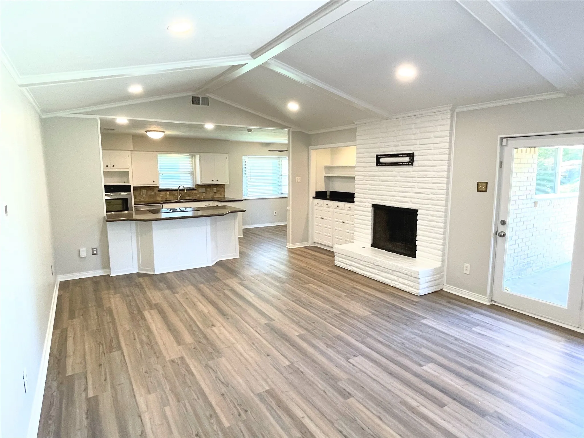 Open concept great room with light wood-type flooring, white cabinetry, oven, and a fireplace